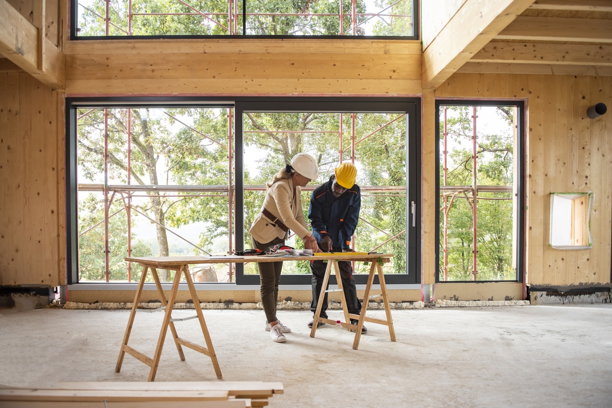 Team of women architect and men construction worker at construction site. They are looking at blueprint.